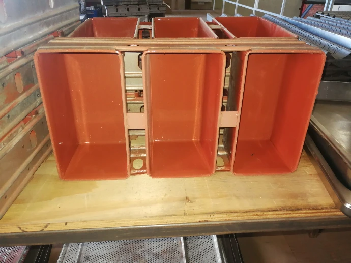 Industrial red silicone or metal baking molds stacked on a wooden workbench shelf in a production facility or bakery.