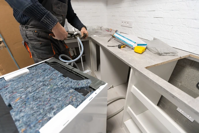 Technician installing water supply hoses for a dishwasher during a kitchen appliance repair or installation service.
