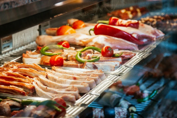 Raw seasoned meats, lamb chops, and skewers garnished with red chili peppers and cherry tomatoes in a butcher display case.